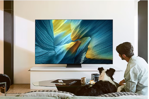 A person and dog sitting on a couch looking at a television AI-generated content may be incorrect.